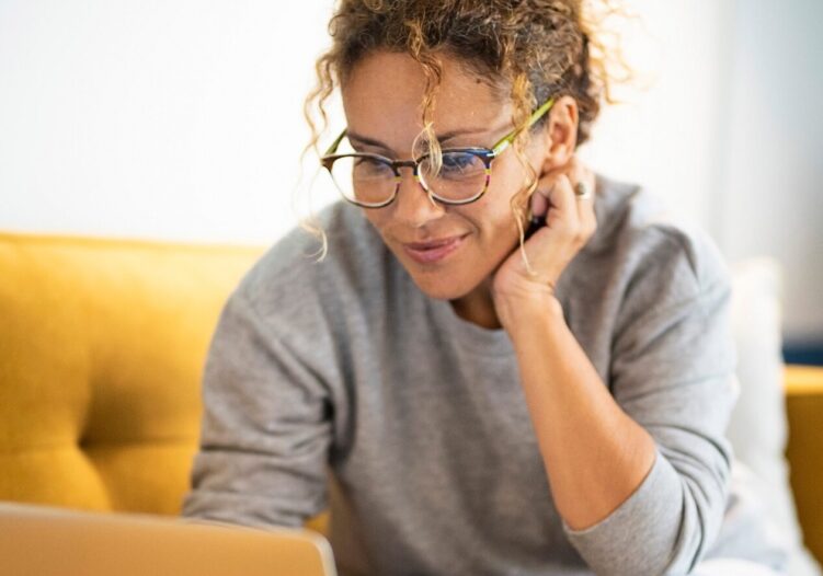 Female adult sat on the sofa reading on a laptop